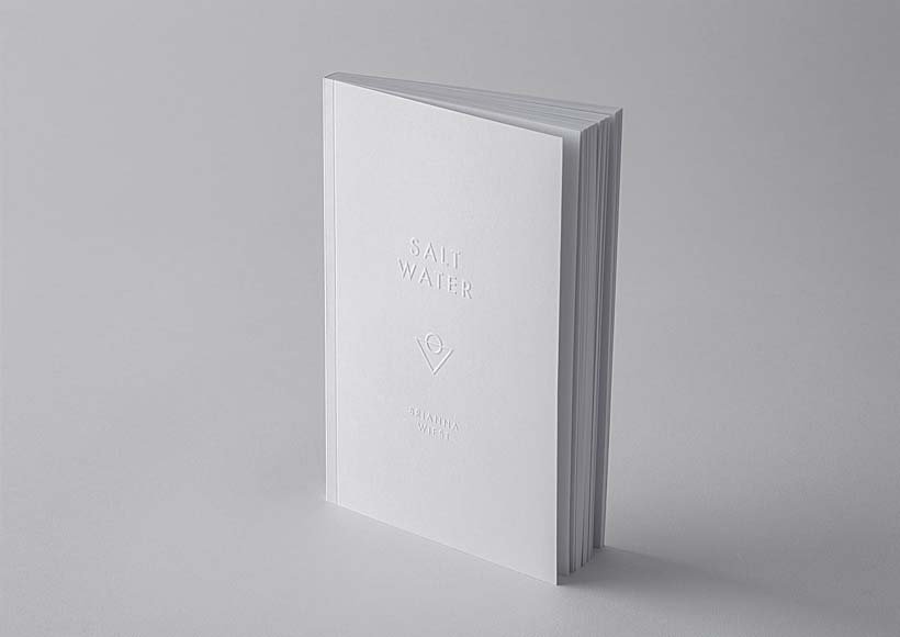 White hardcover book titled salt water standing upright on a gray surface in a minimalist product shot