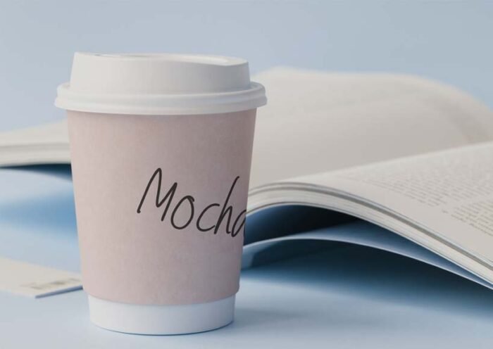To go cup labeled mocha on a desk beside an open magazine