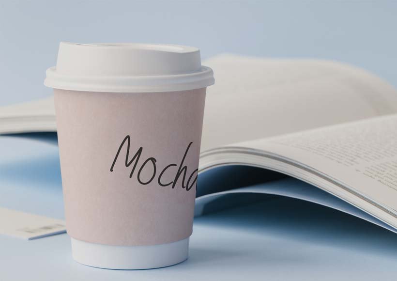 To go cup labeled mocha on a desk beside an open magazine