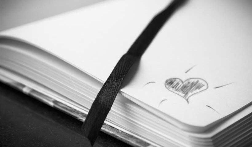 Open notebook with a black ribbon bookmark and a hand-drawn heart on the page.