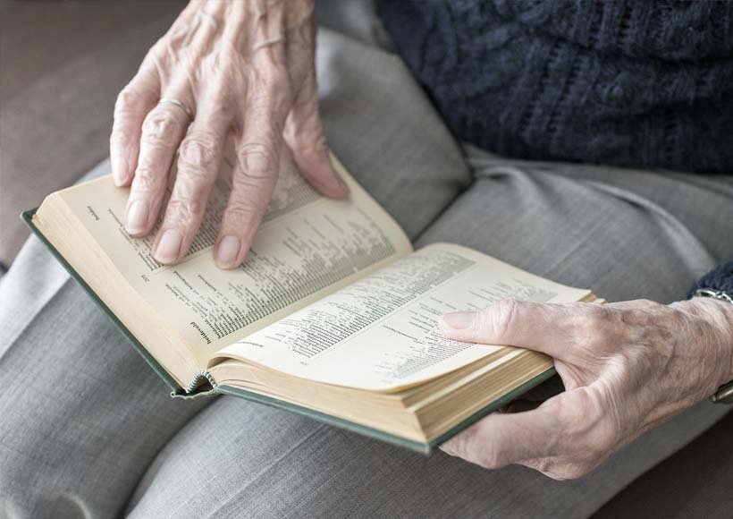 Elderly hands turning the pages of an open hardcover book resting on the lap