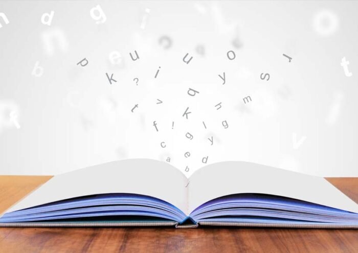 Open book on a wooden table with letters floating upward from its pages