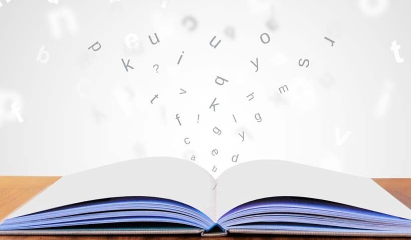 Open book on a wooden table with letters floating upward from its pages