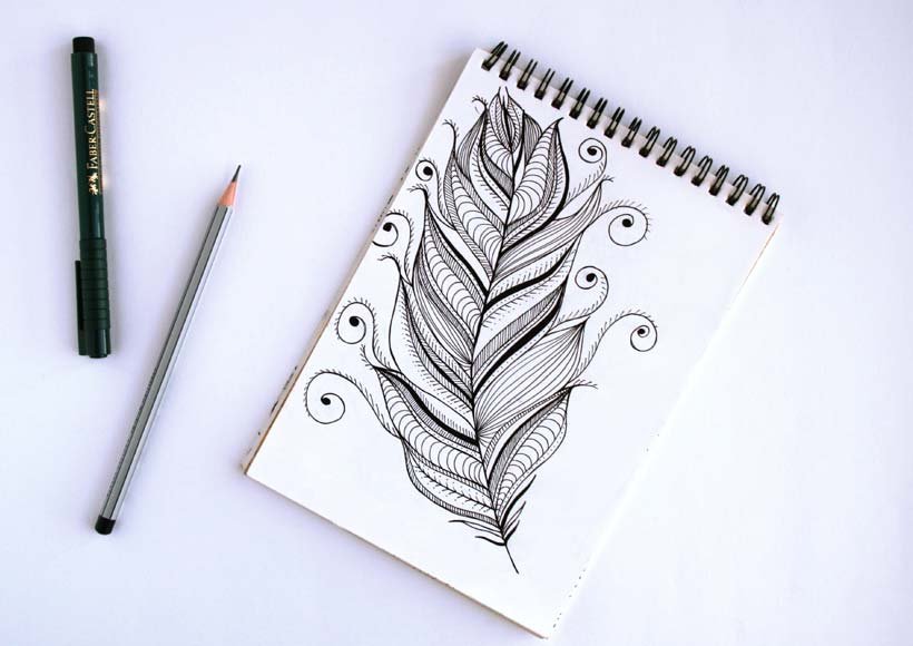 Notebook with a detailed black ink featherleaf doodle a pencil and black marker on a white surface