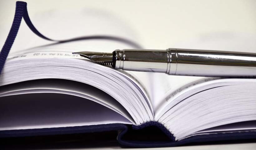 Open hardcover notebook with a silver fountain pen resting on its pages, ready for writing or note-taking.