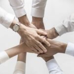 Six hands stacked together in a circle symbolizing teamwork and collaboration
