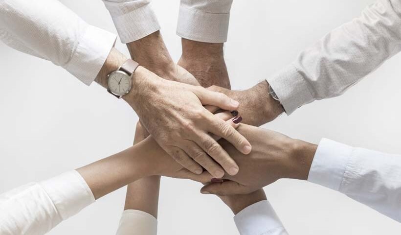 Six hands stacked together in a circle, symbolizing teamwork and collaboration.