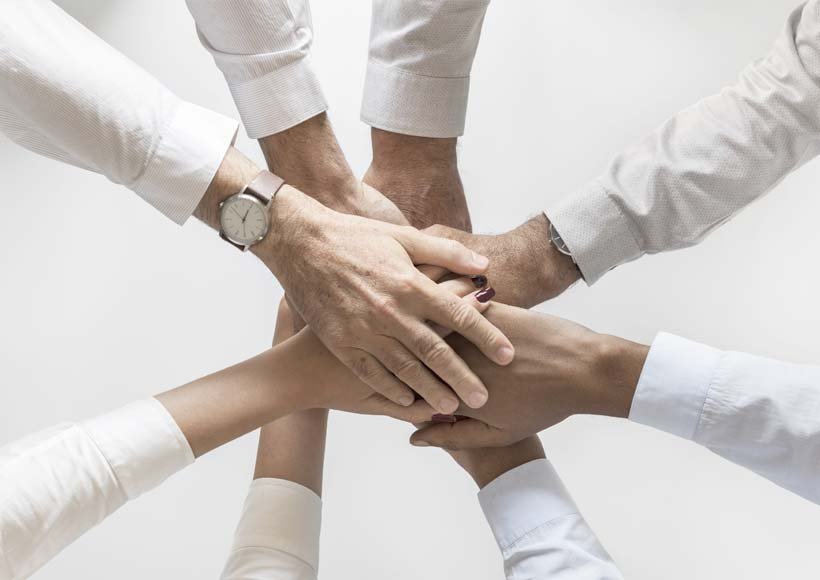 Six hands stacked together in a circle symbolizing teamwork and collaboration
