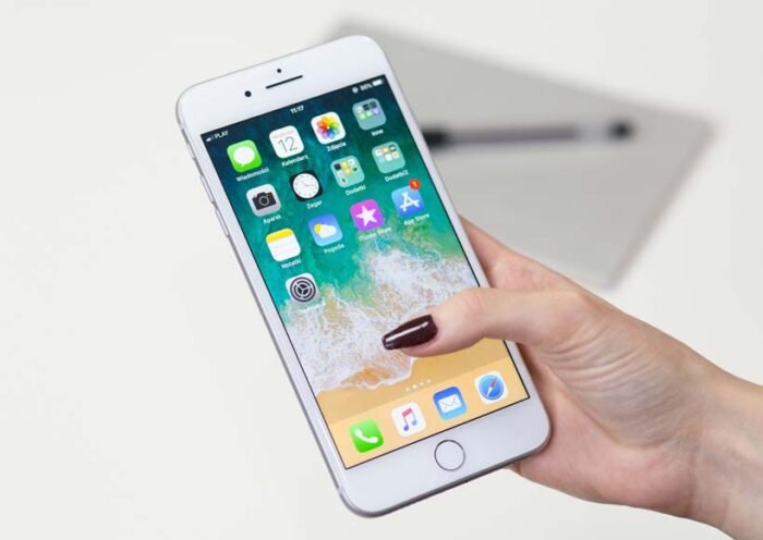 Close up of a hand holding a white iphone displaying the home screen with app icons
