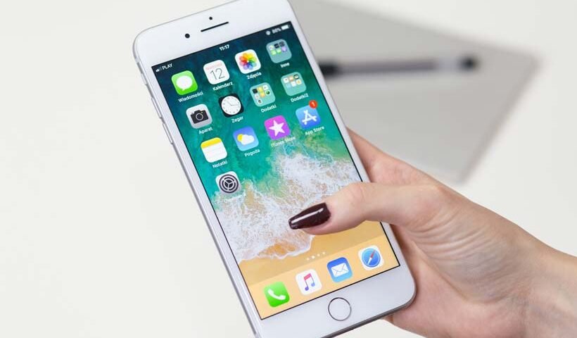 Close-up of a hand holding a white iPhone, displaying the home screen with app icons