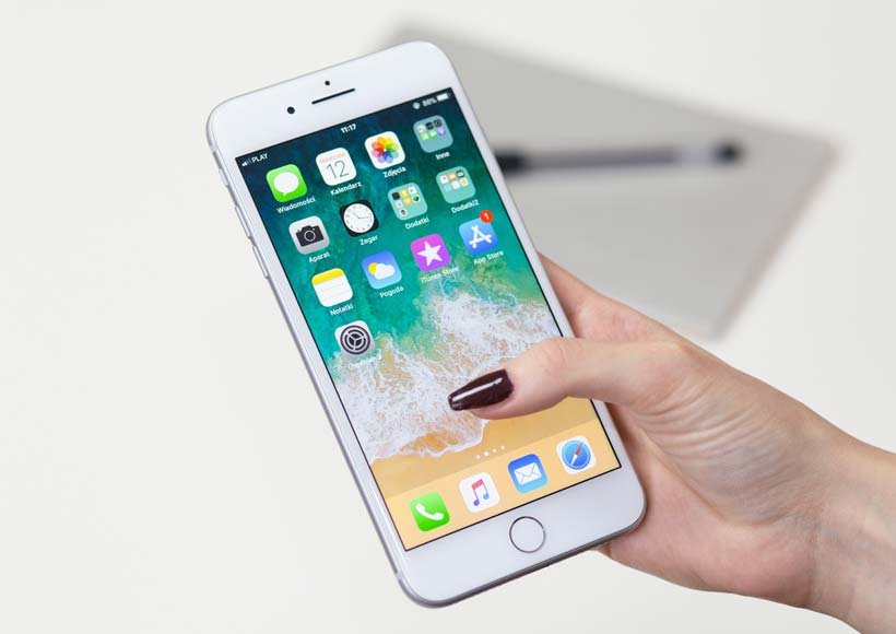 Close up of a hand holding a white iphone displaying the home screen with app icons