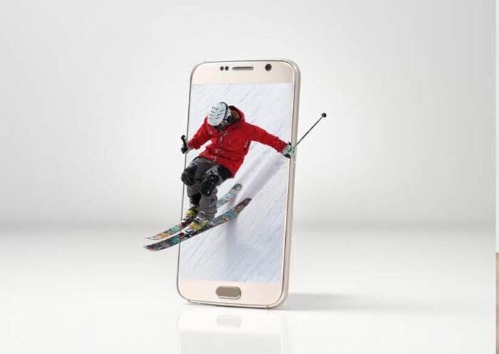 Skier in a red jacket jumps through a smartphone screen as if the phone is a portal to action