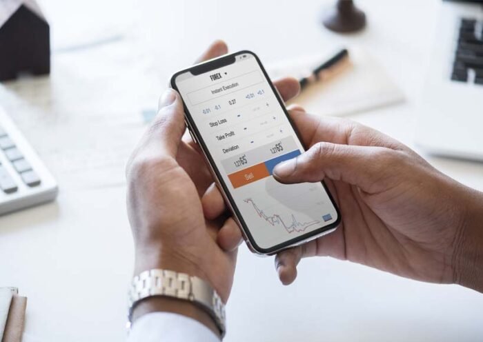 Person holding a phone with a trading app open showing a sell button and a price chart