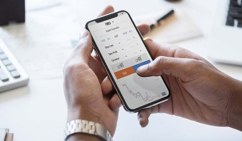 Person holding a phone with a trading app open, showing a Sell button and a price chart.